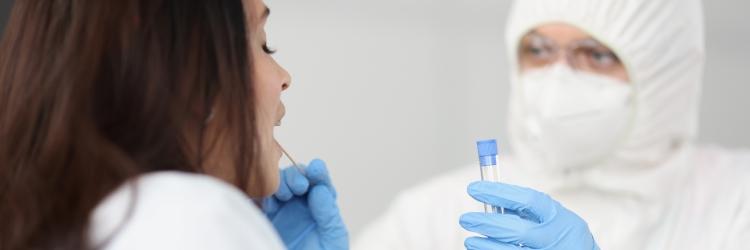 Kvinde får foretaget PCR-test af person med værnemidler.